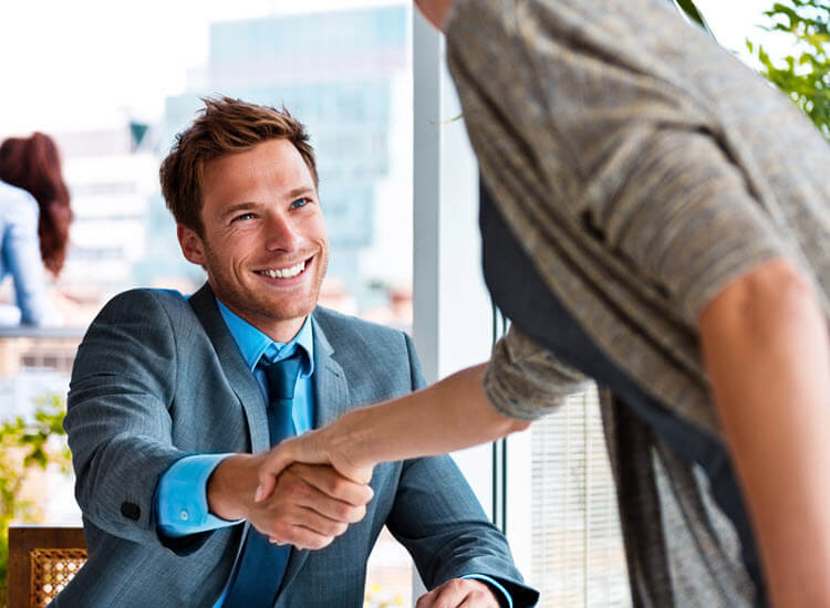 Smiling young businessman sitting in an office and shaking her with his business partner.
