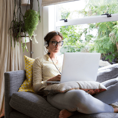 Woman working from home sitting on a sofa working on a laptop wearing a headset