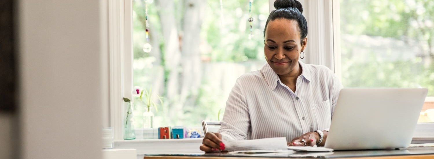Woman sitting at her laptop while looking at a piece of paper