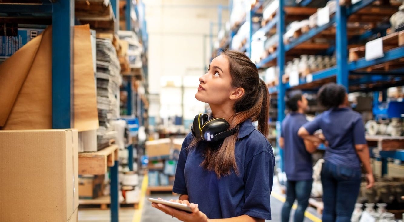 A female factory employee with a digital tablet checking stock levels on shelves in a warehouse.