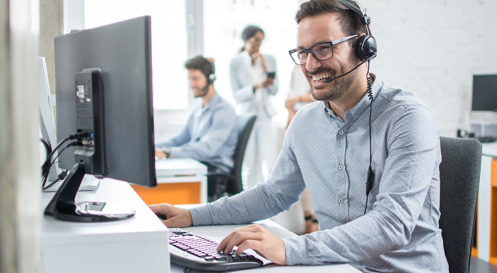 Male call centre worker laughing while talking to customer through his headset