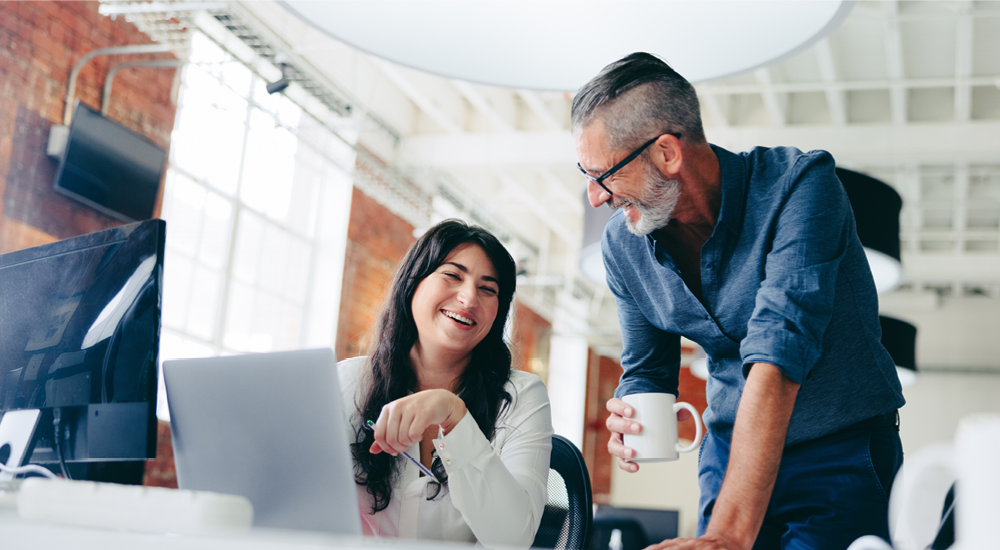 A pair of female and male colleagues laughing while collaborating at work