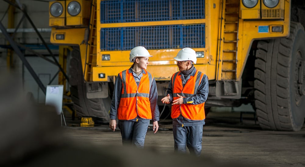 Workers wearing high-visibility safety gear and hard hats beside heavy machinery at an industrial worksite.