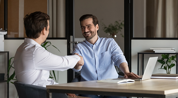 Business man and woman sit at office desk negotiating using laptop discussing ideas