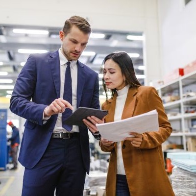 An male businessman showing something on his tablet to a female warehouse manager while standing in a warehouse.