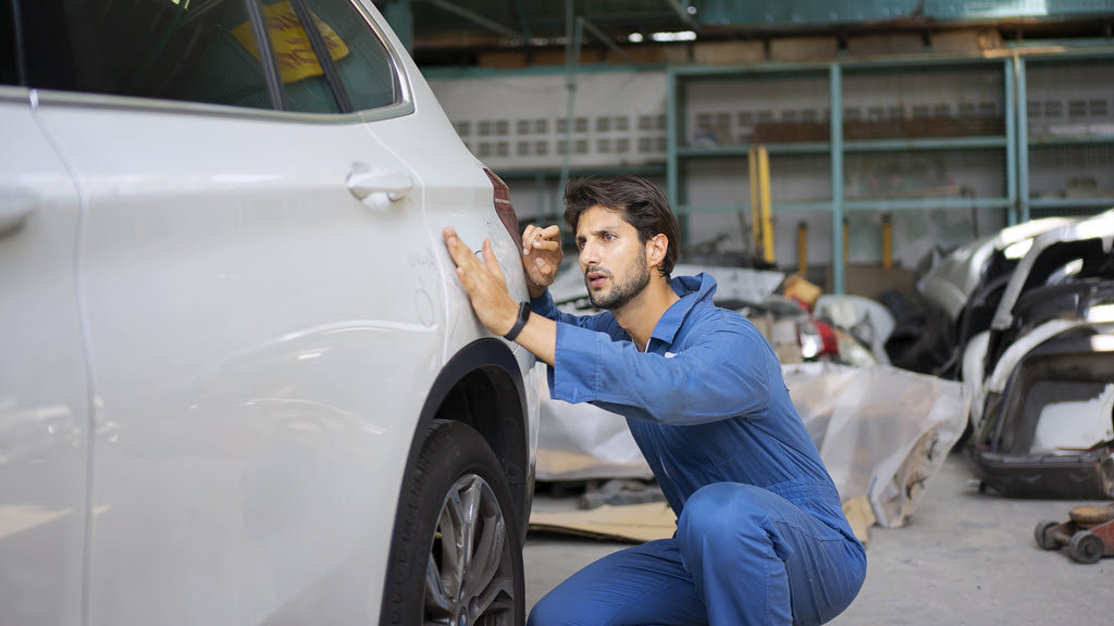 Car repairer checking paint work on repaired car panel