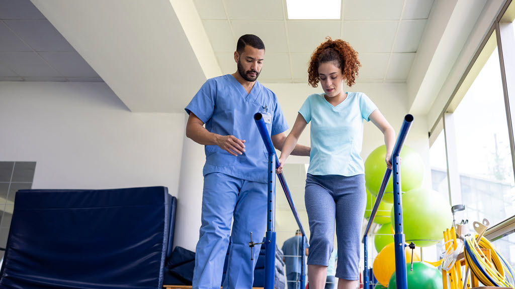 Woman recovering from an injury and walking on bars with the assistance of her physical therapist