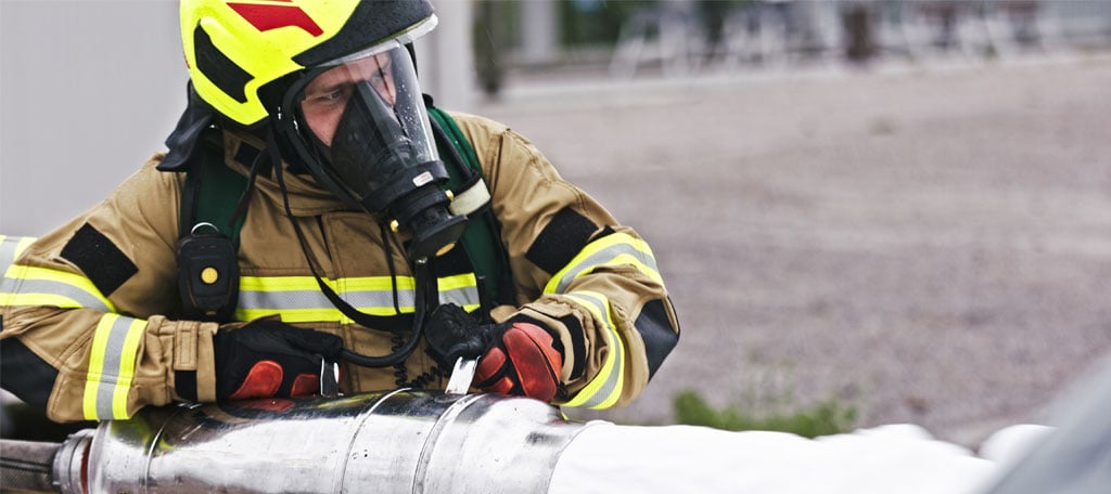 Firefighter in full protective gear operating a large metal hose dispensing firefighting foam