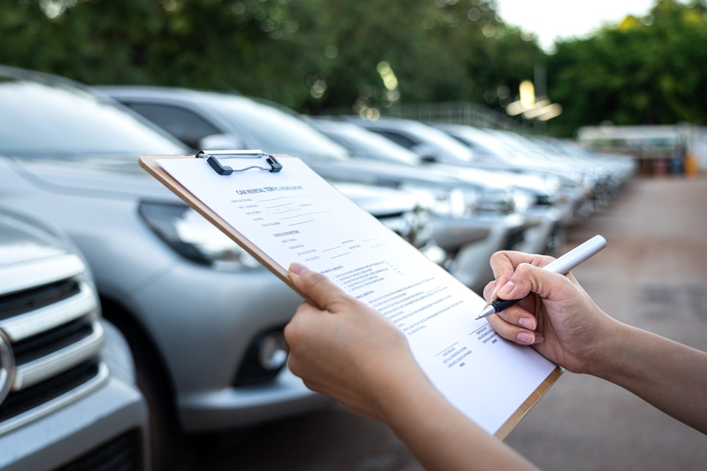 Close up of person checking off items on a clipboard in front of a row of parked cars