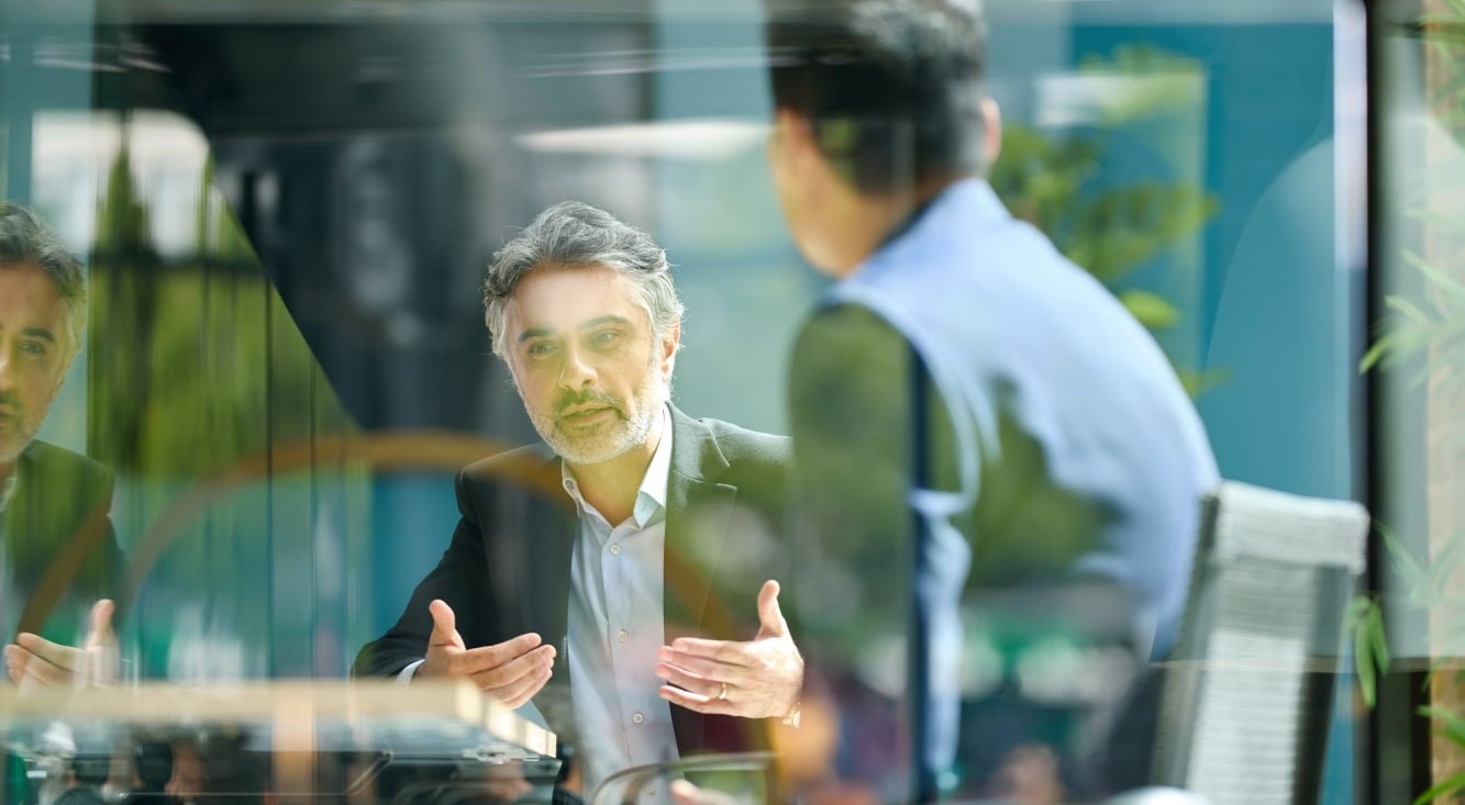 Two people engaged in a business discussion across a meeting table in a glass-walled office