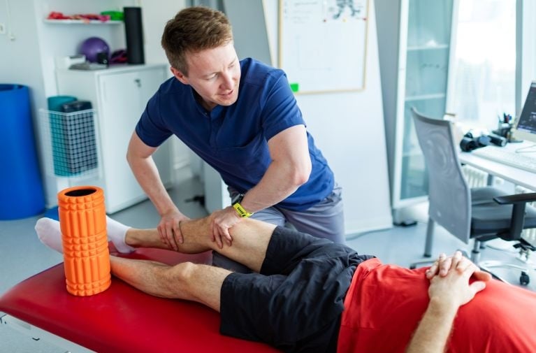 Healthcare practitioner providing leg treatment to a patient lying on an examination table in a clinic