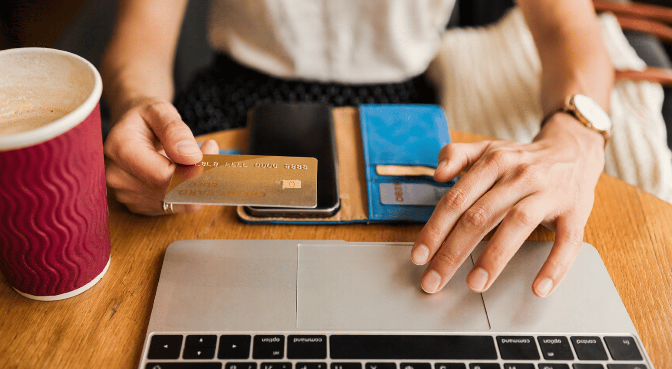 Close-up of a person using a credit card and laptop for an online purchase, with a blue wallet and coffee cup nearby