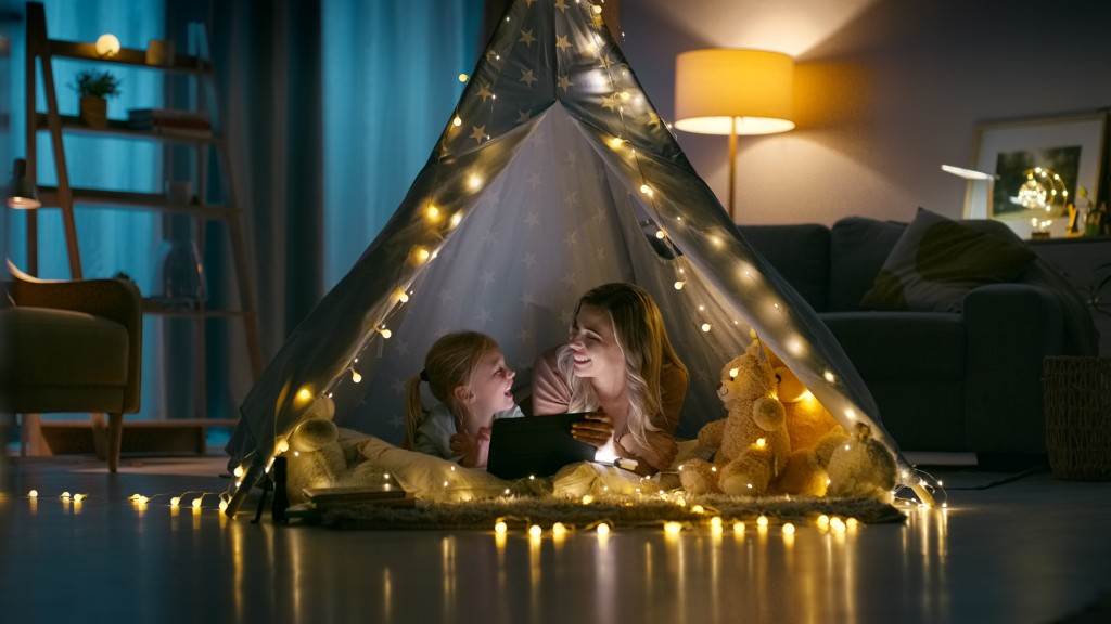 Mother with girl relax at home in a fairy light lit tent in the living room