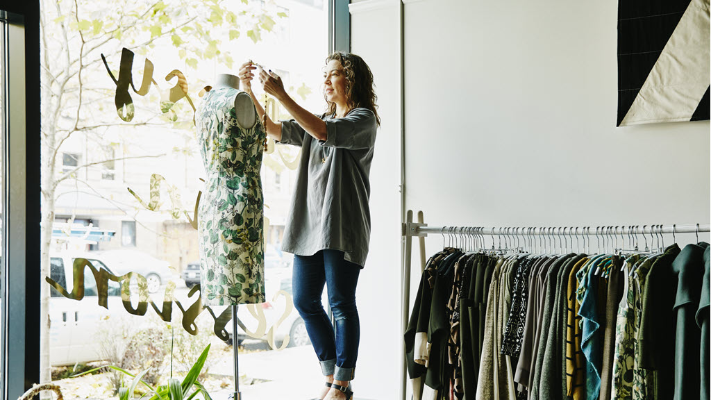 Female business owner dressing dress form in window of boutique