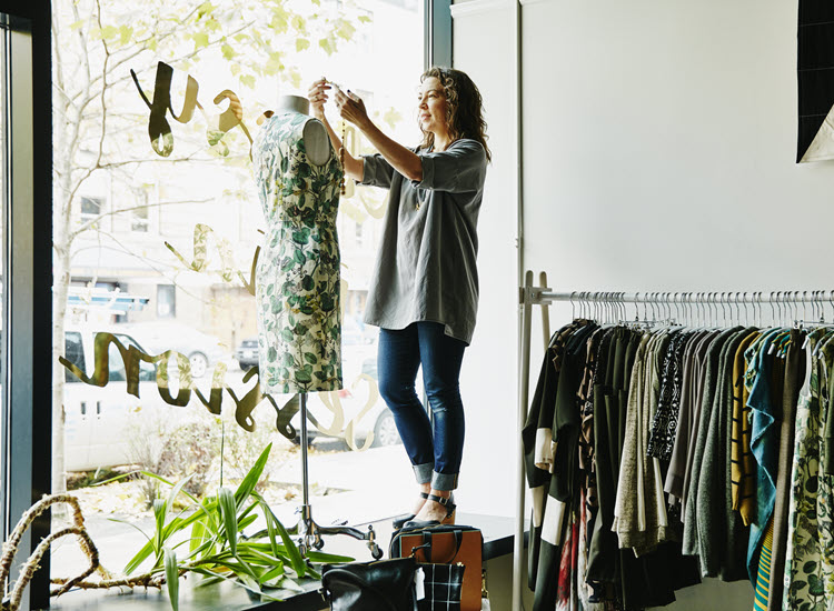 Woman in shop window fitting clothes to mannequin