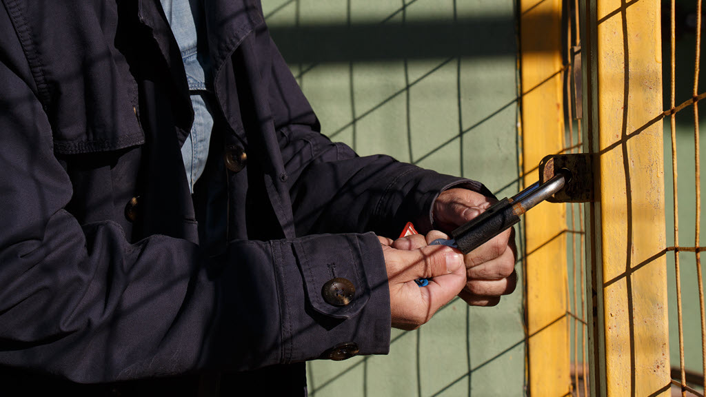 Man opening padlock on metal gates