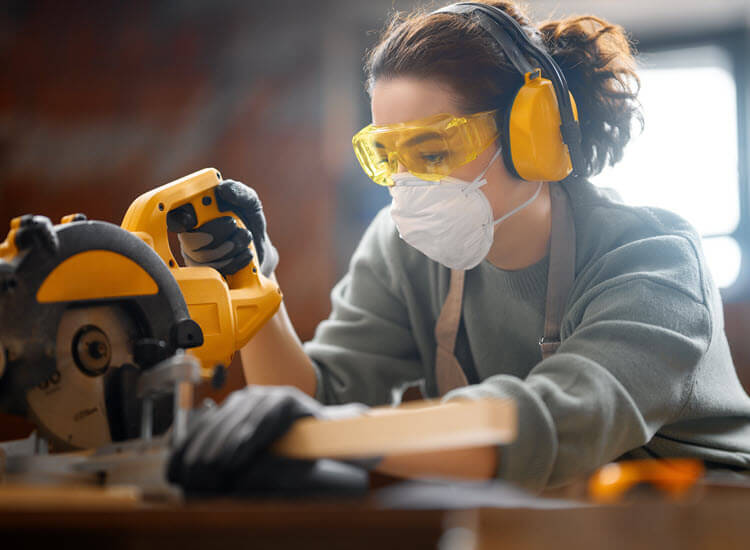 Young female carpenter in workshop wearing appropriate safety gear to operate tools