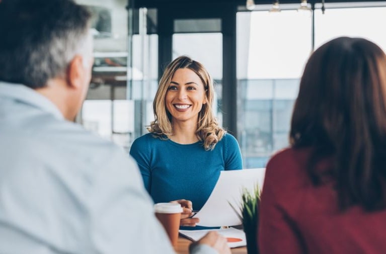 A woman seated with clients around a table reviewing documents, representing a discussion about financial or lending information.