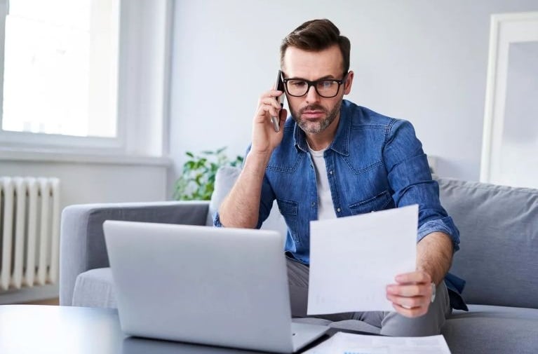 A man seated at home using a laptop and reviewing documents, representing managing a home loan and entering the property market.