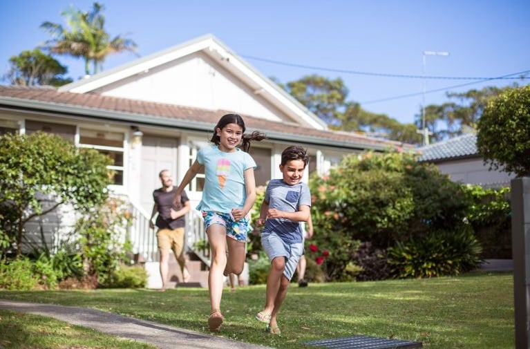 A young family outside a residential home, representing property ownership and mortgage lending scenarios covered by lenders mortgage insurance.