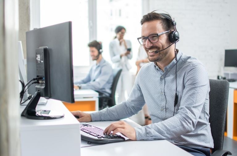 A male customer service team member using a computer and headset in an office environment, representing complaints and feedback support.