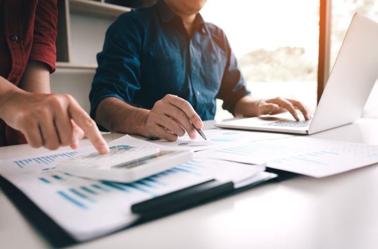 People reviewing financial documents and data on a laptop, representing credit history checks as part of the lenders mortgage insurance assessment process.