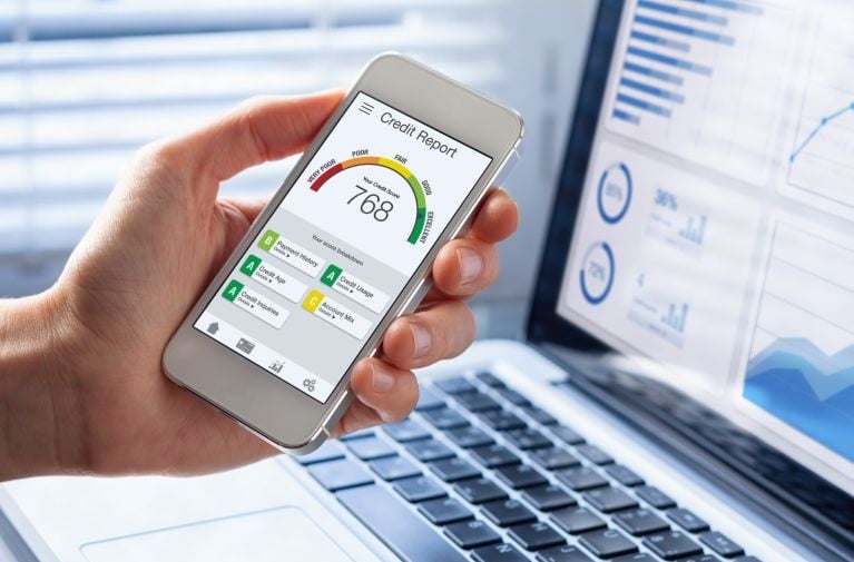Credit report score shown on a smartphone alongside a laptop with financial data, illustrating credit history assessment.