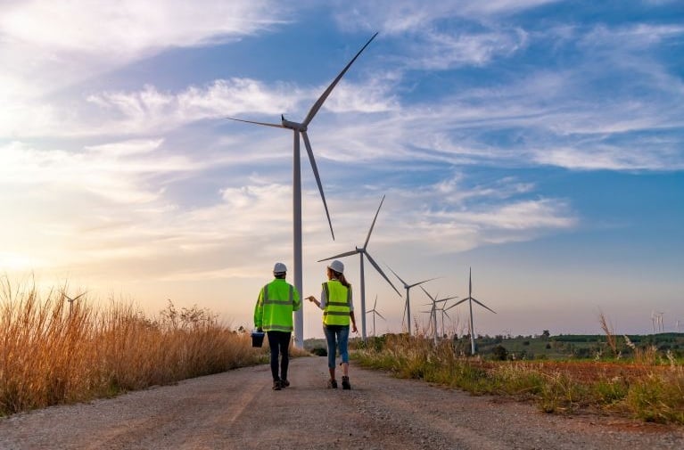 Wind turbines in a rural landscape with people walking along a path, representing renewable energy and positive environmental impact.