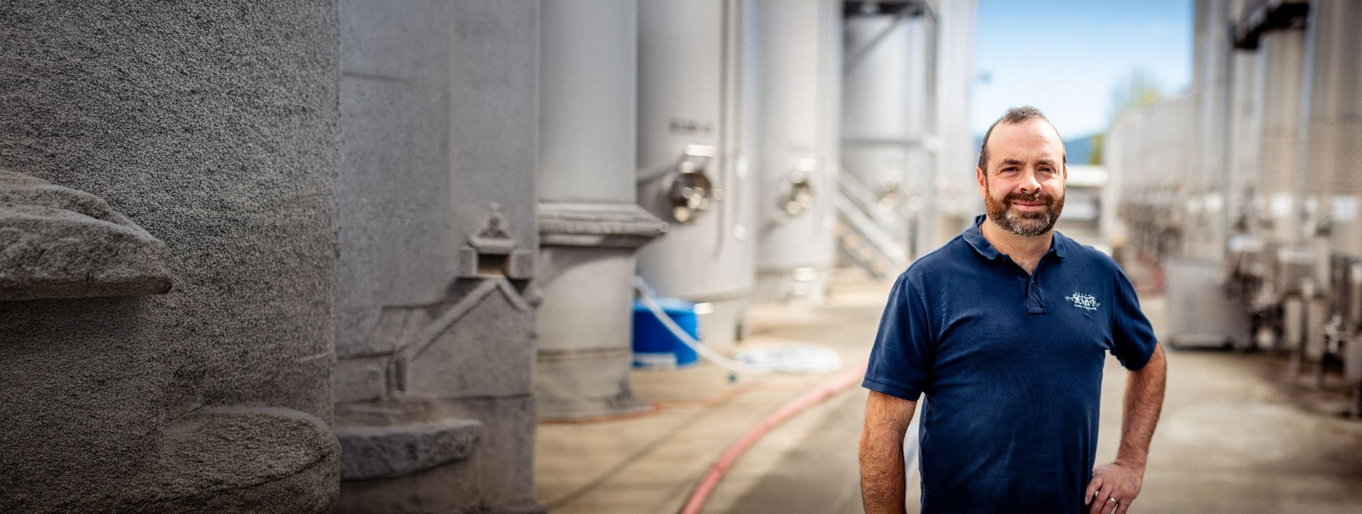 A man standing at an industrial facility with large metal tanks in the background