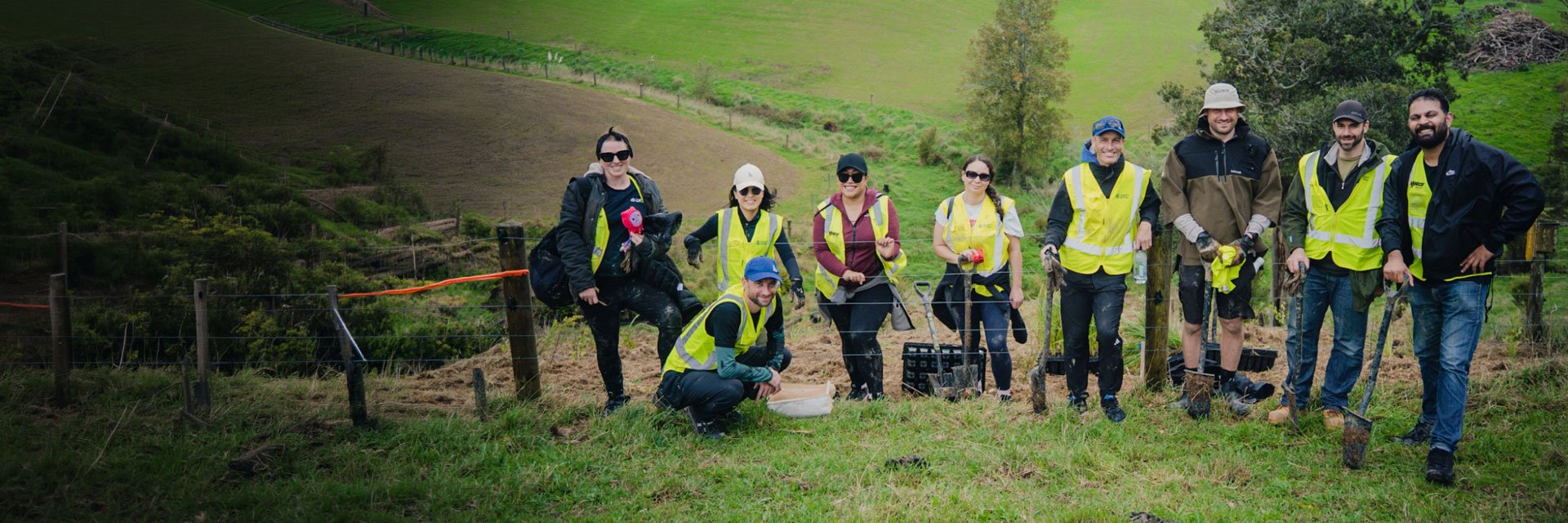 A group of people wearing high-visibility vests taking part in outdoor conservation and planting work in a rural landscape