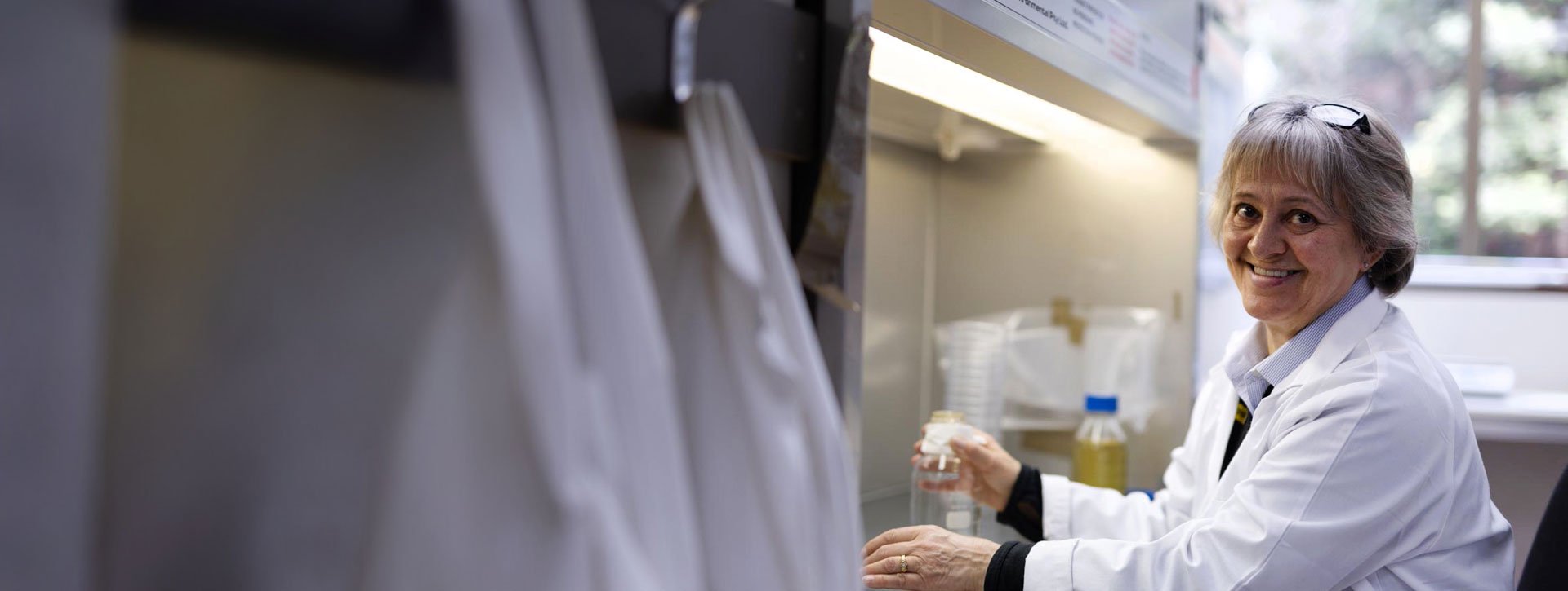 A woman working in a laboratory, handling sample containers under a lab hood