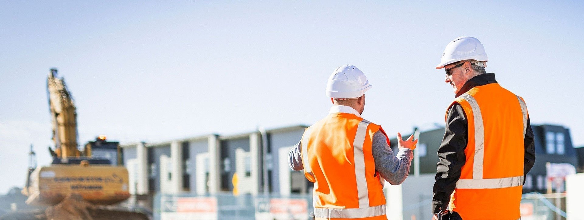 Rear view of two workers wearing high‑visibility vests and helmets standing at a construction site
