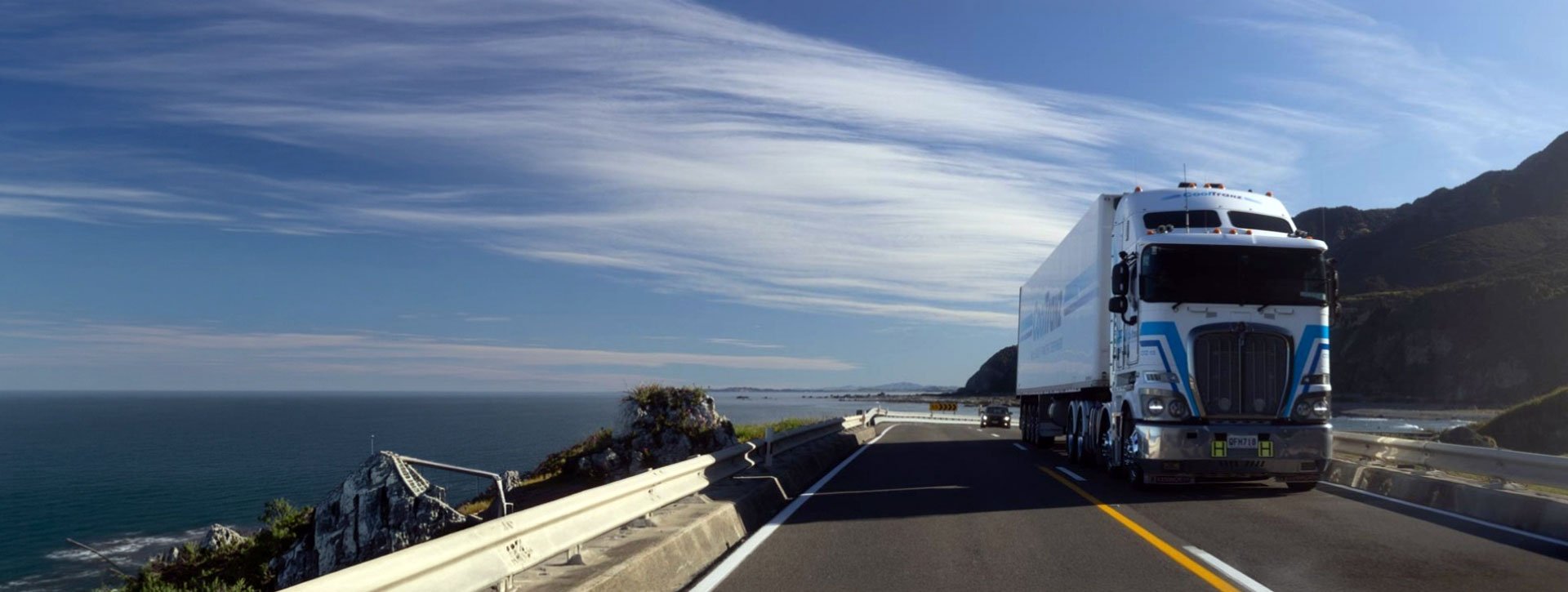A large commercial truck driving on a highway through a coastal landscape