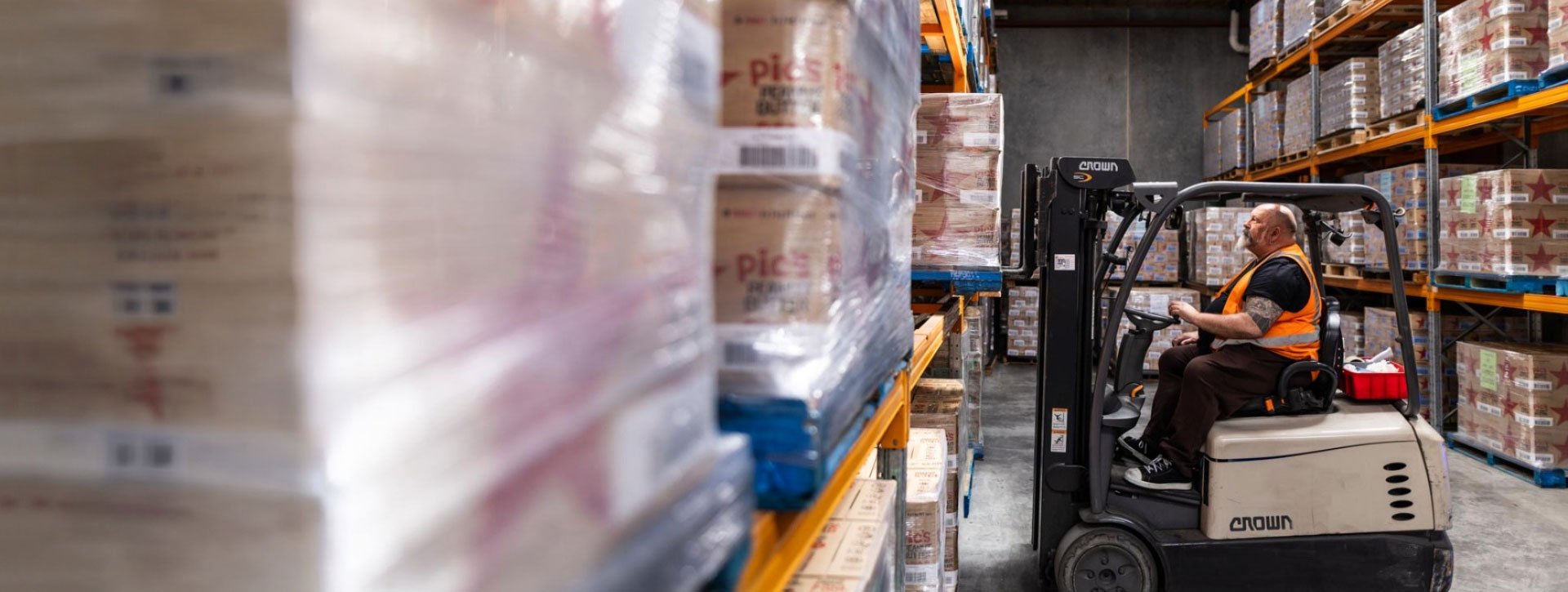 Warehouse worker operating a forklift to move palletised goods in a storage facility.
