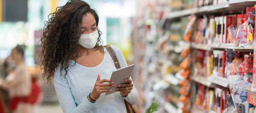 woman at a supermarket with a mask on using a tablet