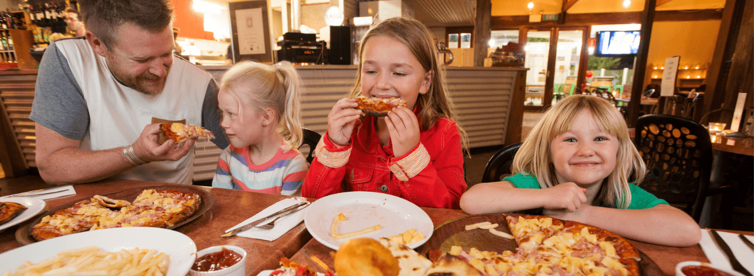 Dad and his three young daughters in a restaurant eating pizza