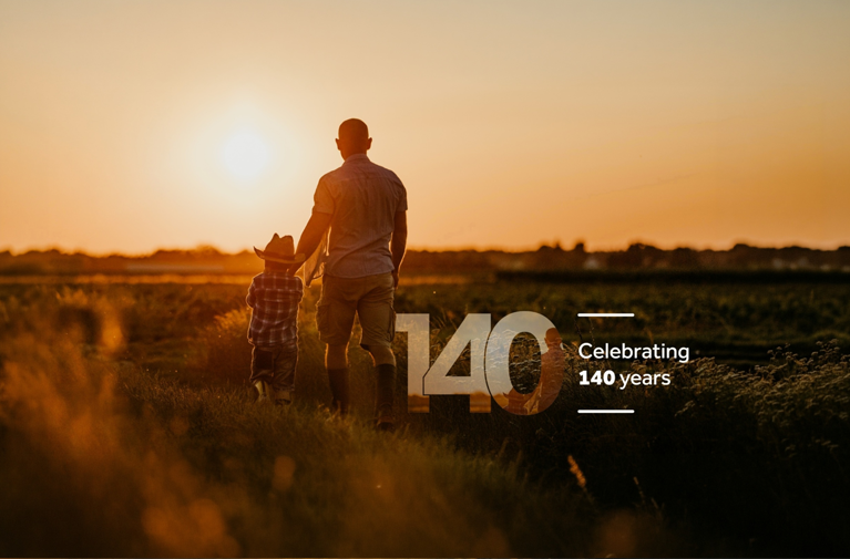 Rear view of a man and child walking through a rural field at sunset, celebrating QBE's 140 years of supporting Australians