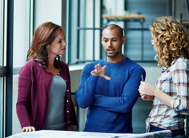 Three business colleagues stand together in the office discussing a project