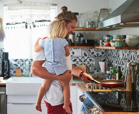 Father carrying daughter while cooking food in kitchen