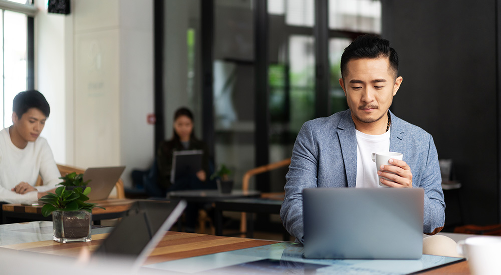 man holding coffee cup looking at his laptop